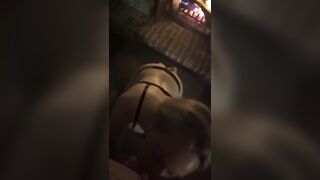 Blond in ebony belt gives fellatio by a fire