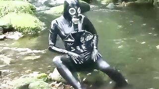 Outdoor walk in the wood and river washroom full encased in ebony latex catsuit and rubber gas mask